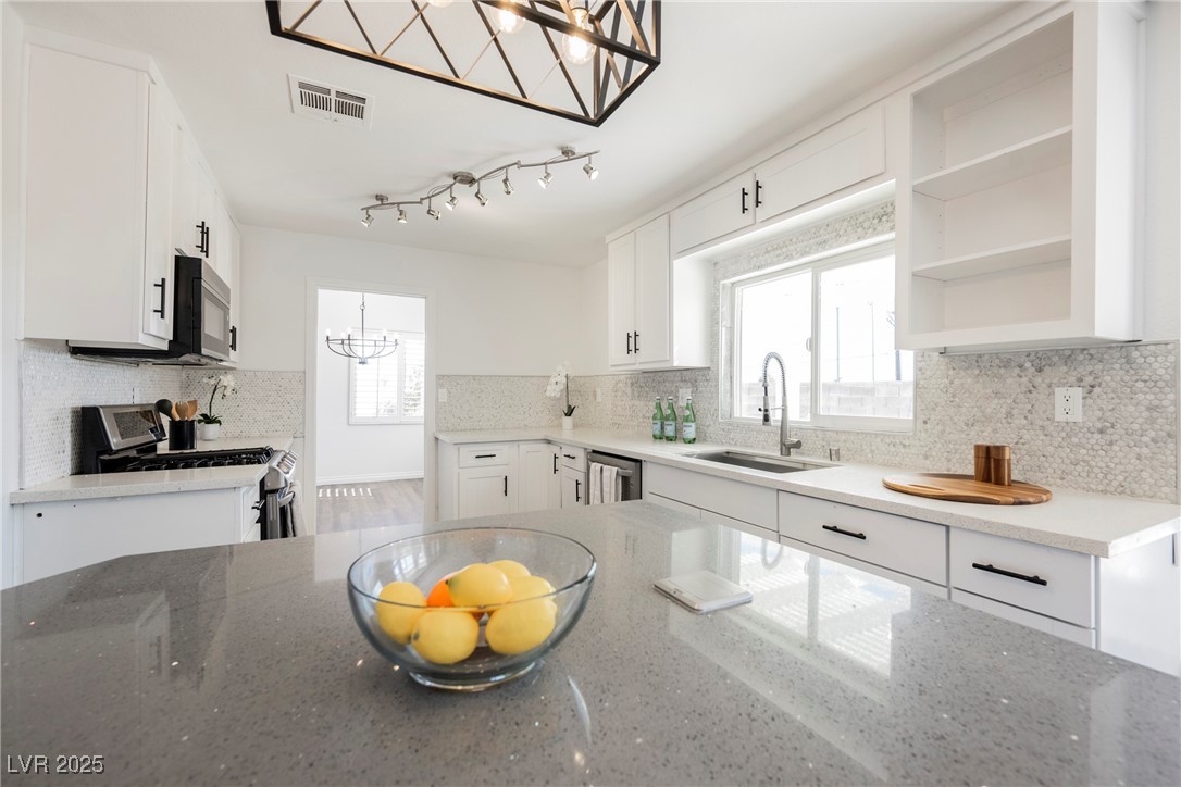 1706 Toltec Circle Henderson, NV 89014 - Photo 12 of 21 Kitchen featuring light stone counters, a chandelier, backsplash, stainless steel appliances, and open shelves