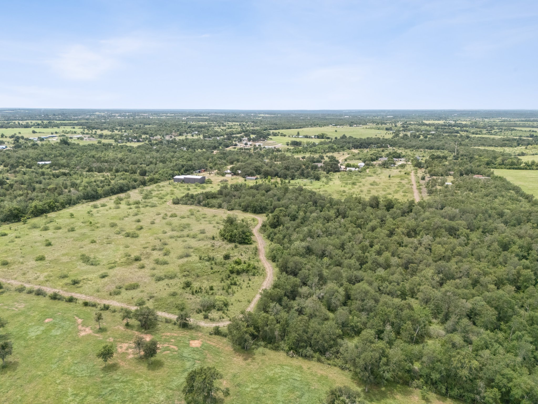 406 Monkey Road Elgin, TX 78621 - Photo 34 of 39 Expansive acreage featuring mature trees, open clearings, and a substantial outbuilding with a metal roof
