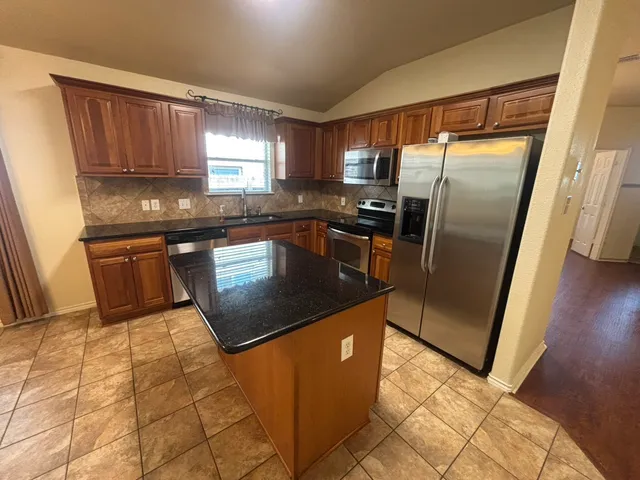 a kitchen with stainless steel appliances granite countertop a refrigerator a sink a stove a washer dryer and a window