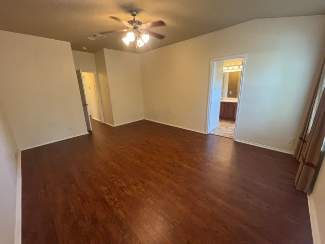 a view of an empty room with wooden floor and a ceiling fan