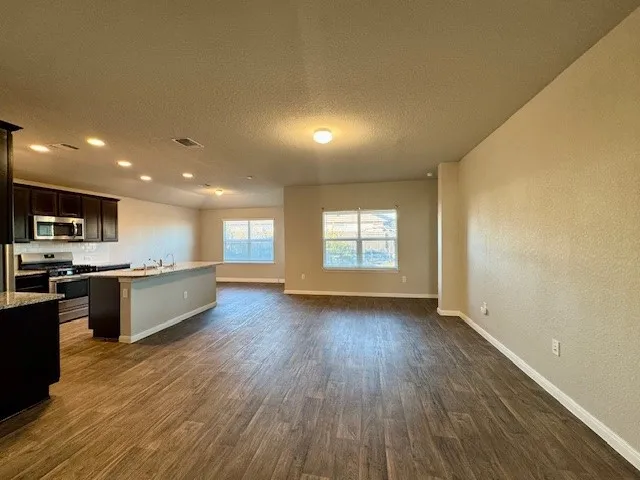 a kitchen with stainless steel appliances granite countertop a sink a stove a refrigerator cabinets and a wooden floor