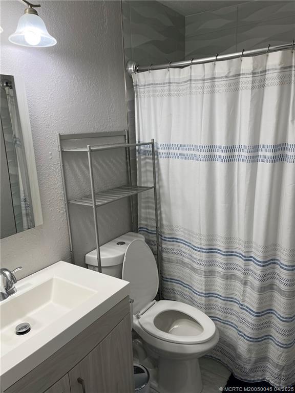 2340 Northeast Rustic Way Jensen Beach, FL 34957 - Photo 13 of 19 a bathroom with a sink a toilet a mirror and shower curtain