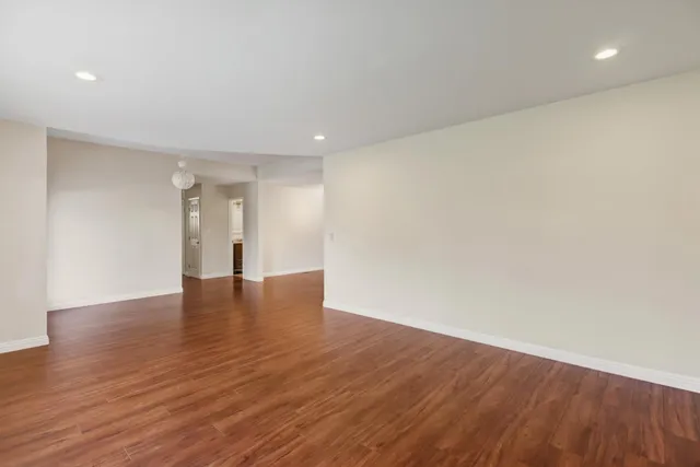 a view of an empty room with wooden floor and a ceiling fan