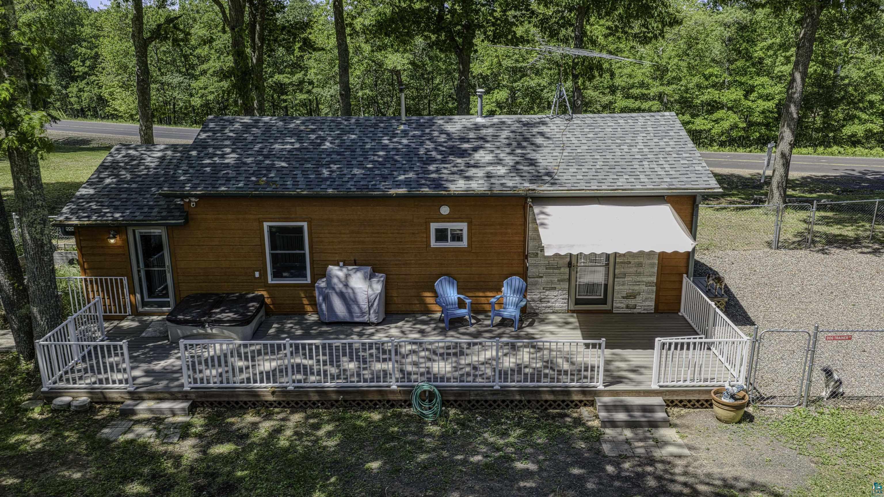 66075 Rooster Road Iron River, WI 54847 - Photo 4 of 52 Wood-sided exterior featuring an expansive outdoor deck, white railing, a built-in hot tub, and a stone facade section under a retractable awning