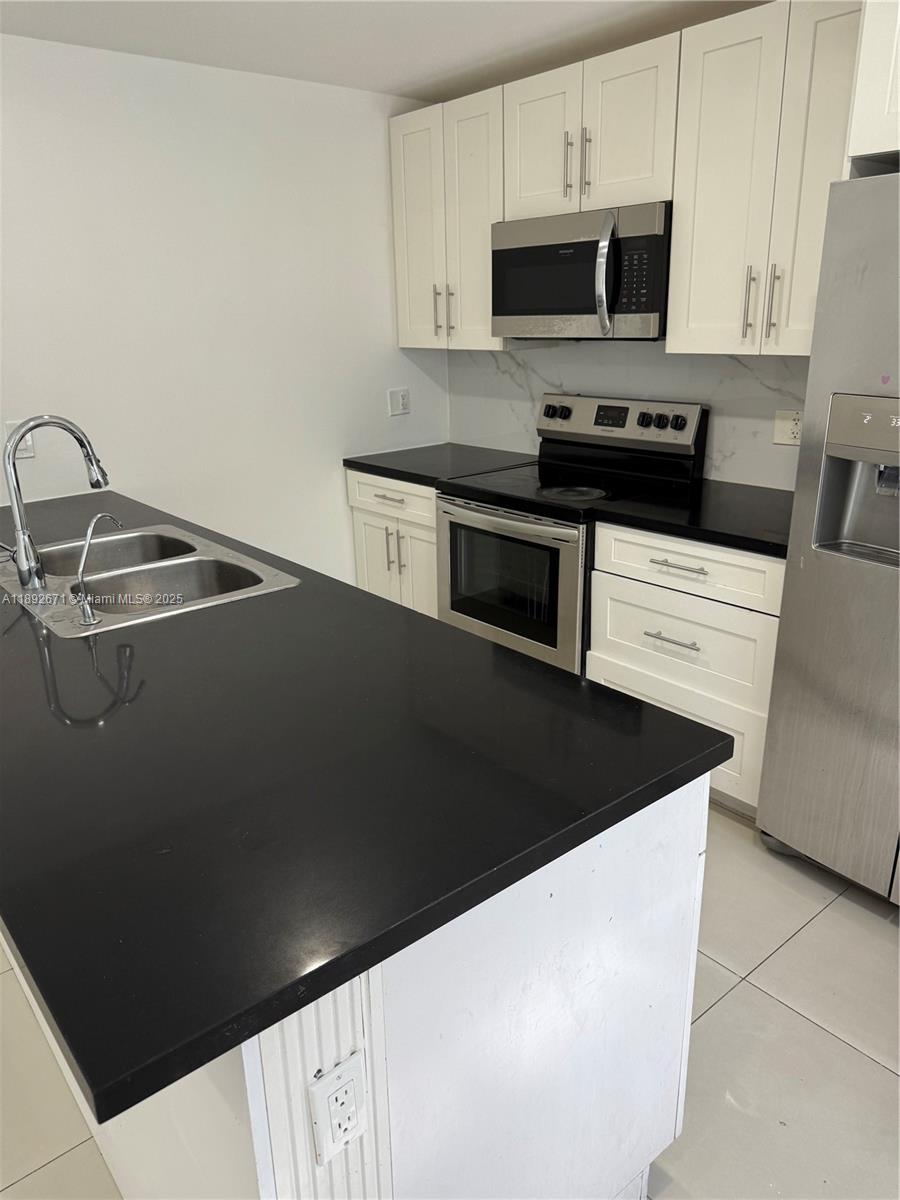13984 Southwest 259th Street, Unit 13984 Homestead, FL 33032 - Photo 63 of 67 a kitchen with stainless steel appliances a sink a stove a microwave and cabinets