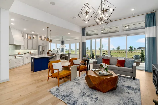 a living room with lots of furniture kitchen view and a large window