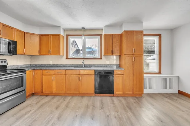 a kitchen with granite countertop wooden floors stainless steel appliances a sink and a window