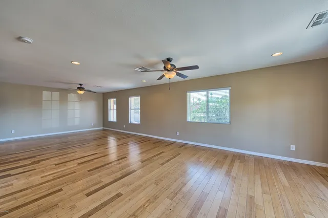 an empty room with wooden floor chandelier fan and windows