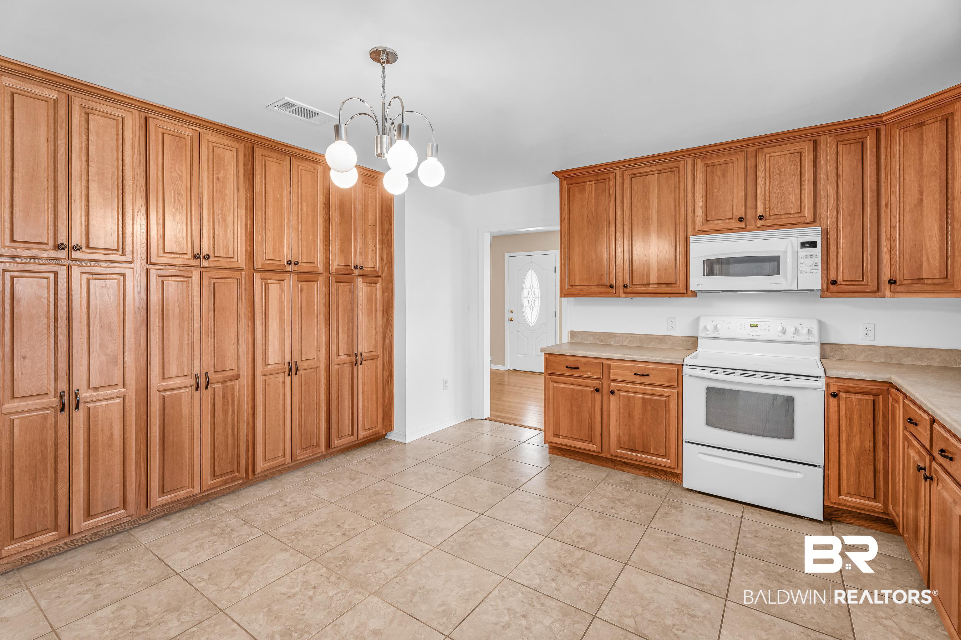 22095 8th Street Silverhill, AL 36576 - Photo 22 of 42 Kitchen with white appliances, a chandelier, wood finish cabinets, light countertops, and light tile patterned floors