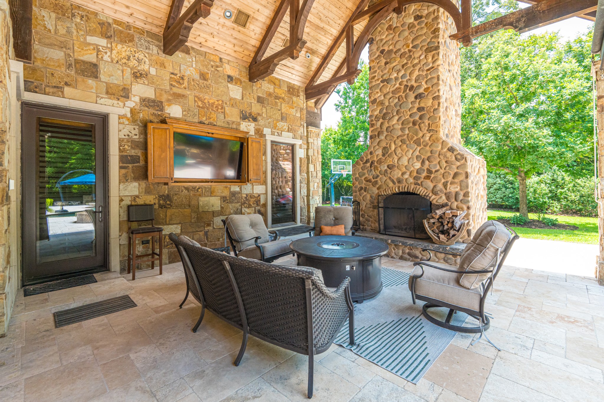 247 South Fazio Way Spring, TX 77389 - Photo 15 of 17 Designed for year-round enjoyment, this spacious outdoor living room features a floor-to-ceiling stone fireplace, mounted TV, soaring wood-beamed ceilings, and comfortable gathering spaces overlooking the resort-style backyard.