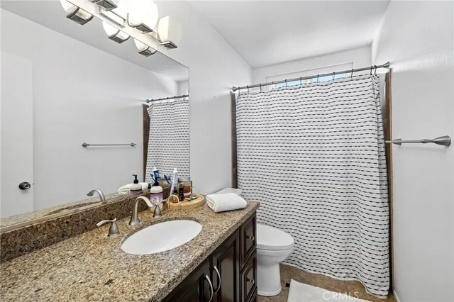 a bathroom with a granite countertop sink a toilet a mirror and shower curtain