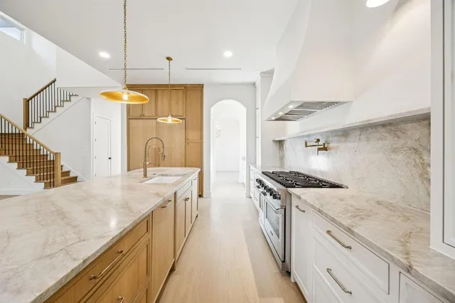 a kitchen with granite countertop a sink a stove top oven and cabinetry