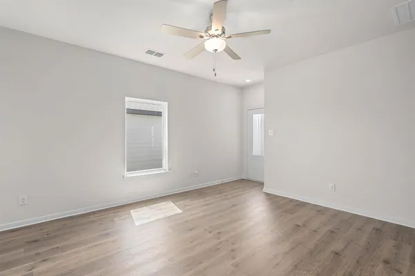 an empty room with wooden floor chandelier fan and windows