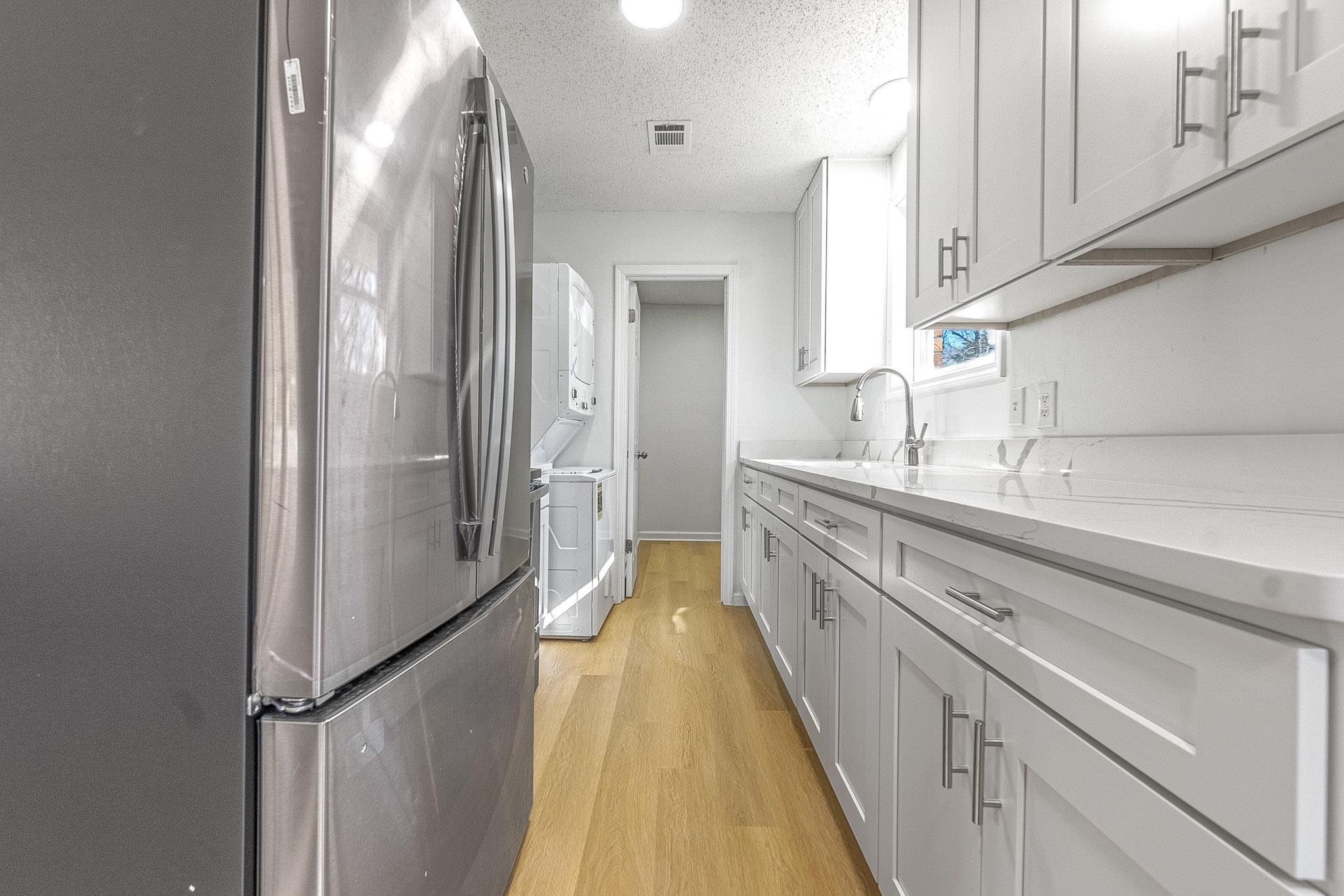 1165 Clift Road Bolivar, TN 38008 - Photo 22 of 26 Kitchen featuring freestanding refrigerator, light wood finished floors, a textured ceiling, light stone counters, and estacked washer and dryer