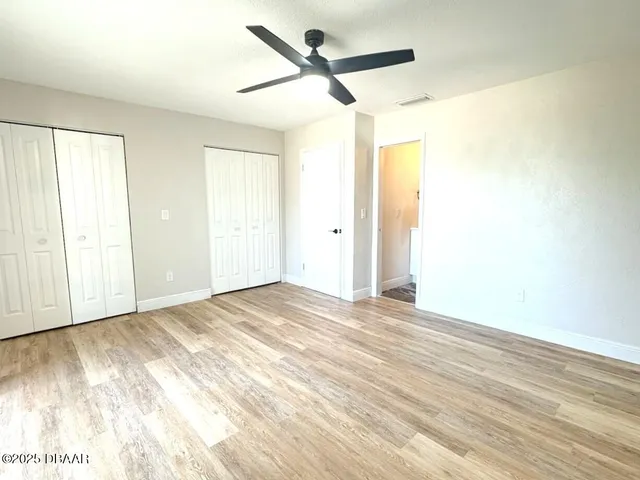 an empty room with wooden floor fan and windows