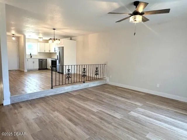 a view of a room with wooden floor ceiling fan and kitchen view