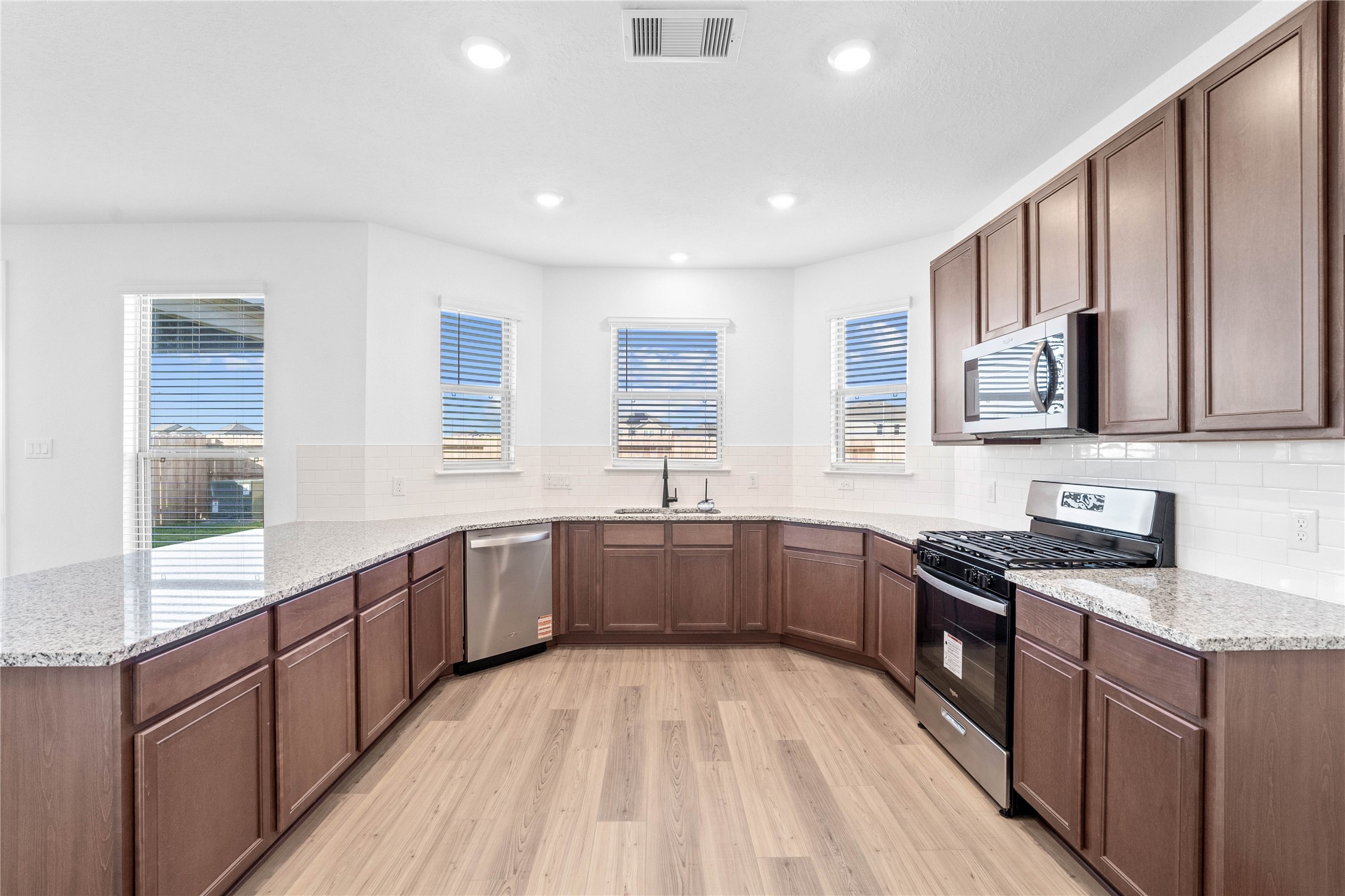 6410 Kentfield Drive Rosharon, TX 77583 - Photo 8 of 25 This spacious kitchen boasts high ceilings, Woodmont Cody cabinets in a Ginger stain, Granite Luna Pearl countertops, stainless steel Whirlpool appliances, a modern Daltile backsplash, recessed lighting, windows with blinds, an added breakfast bar to kitchen countertop, and a pantry—all overlooking the expansive Great Room.
