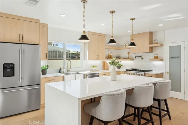 a kitchen with stainless steel appliances a stove a sink a kitchen island with chairs refrigerator and cabinets