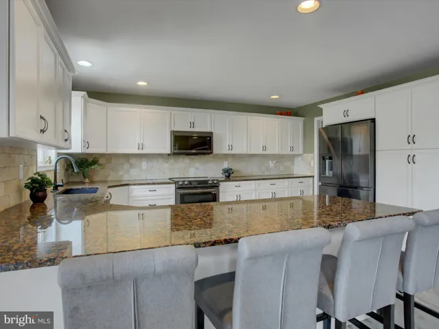 a kitchen with stainless steel appliances granite countertop a stove top oven a sink a refrigerator white cabinets and granite countertops with wooden floor