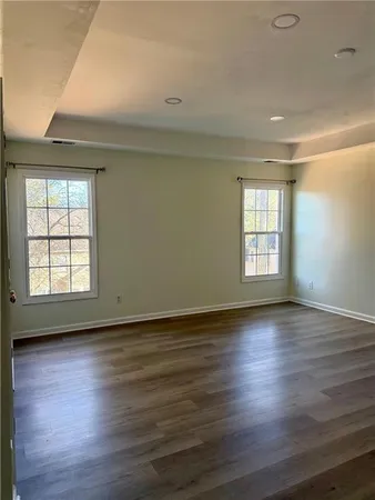 an empty room with wooden floor and windows with curtains