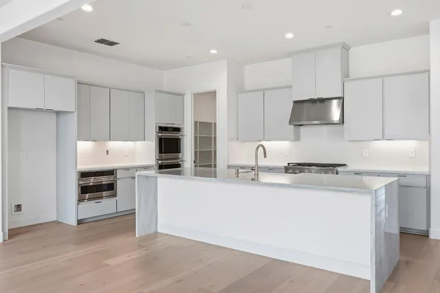 a kitchen with stainless steel appliances granite countertop a stove top oven a sink a refrigerator and white cabinets with wooden floor