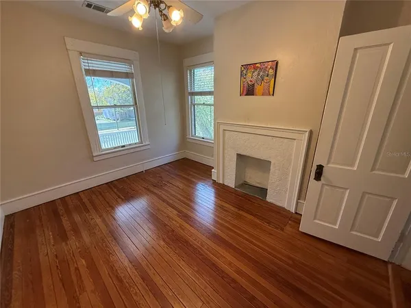 an empty room with wooden floor fireplace and windows