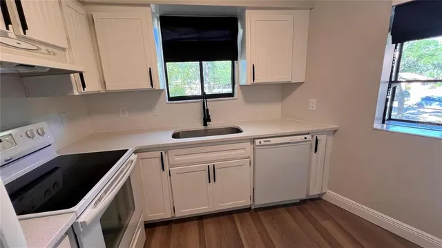 a kitchen with white cabinets a sink dishwasher and a stove with wooden floor