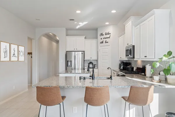 a kitchen with stainless steel appliances kitchen island granite countertop a dining table chairs and a refrigerator