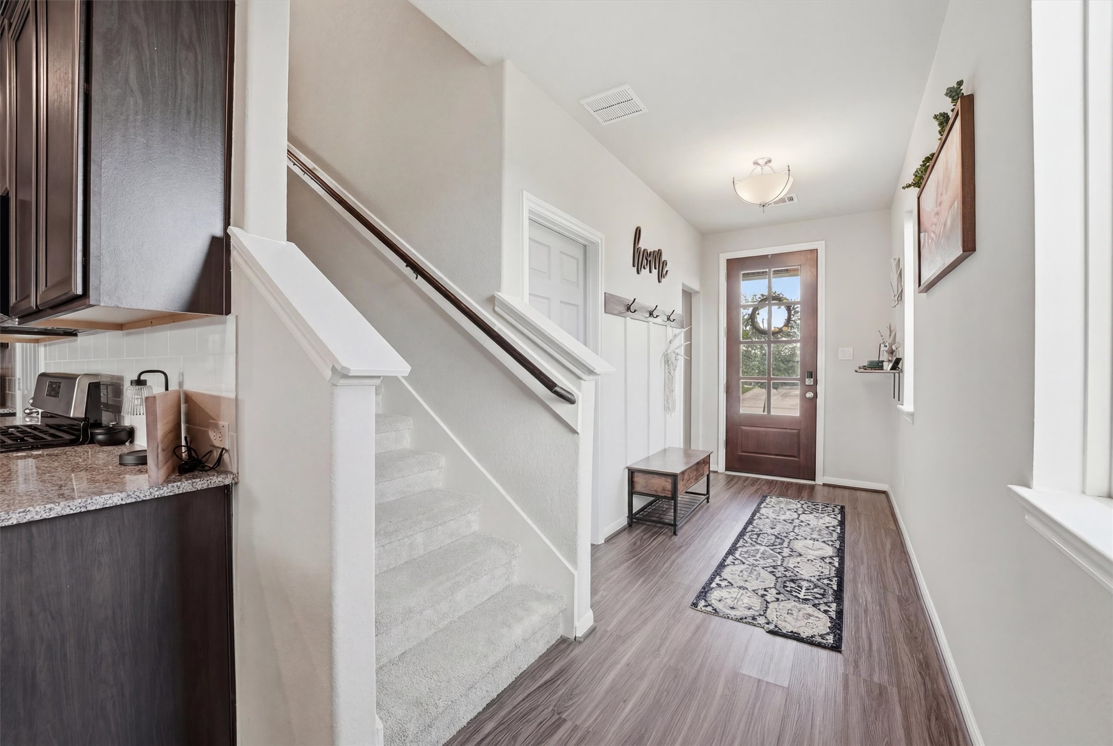 2130 Shellbark Way La Marque, TX 77568 - Photo 4 of 30 Welcoming foyer features a wooden front door with glass panels. The staircase leads upstairs, and the adjacent kitchen showcases dark cabinetry and granite countertops, blending functionality with modern elegance.
