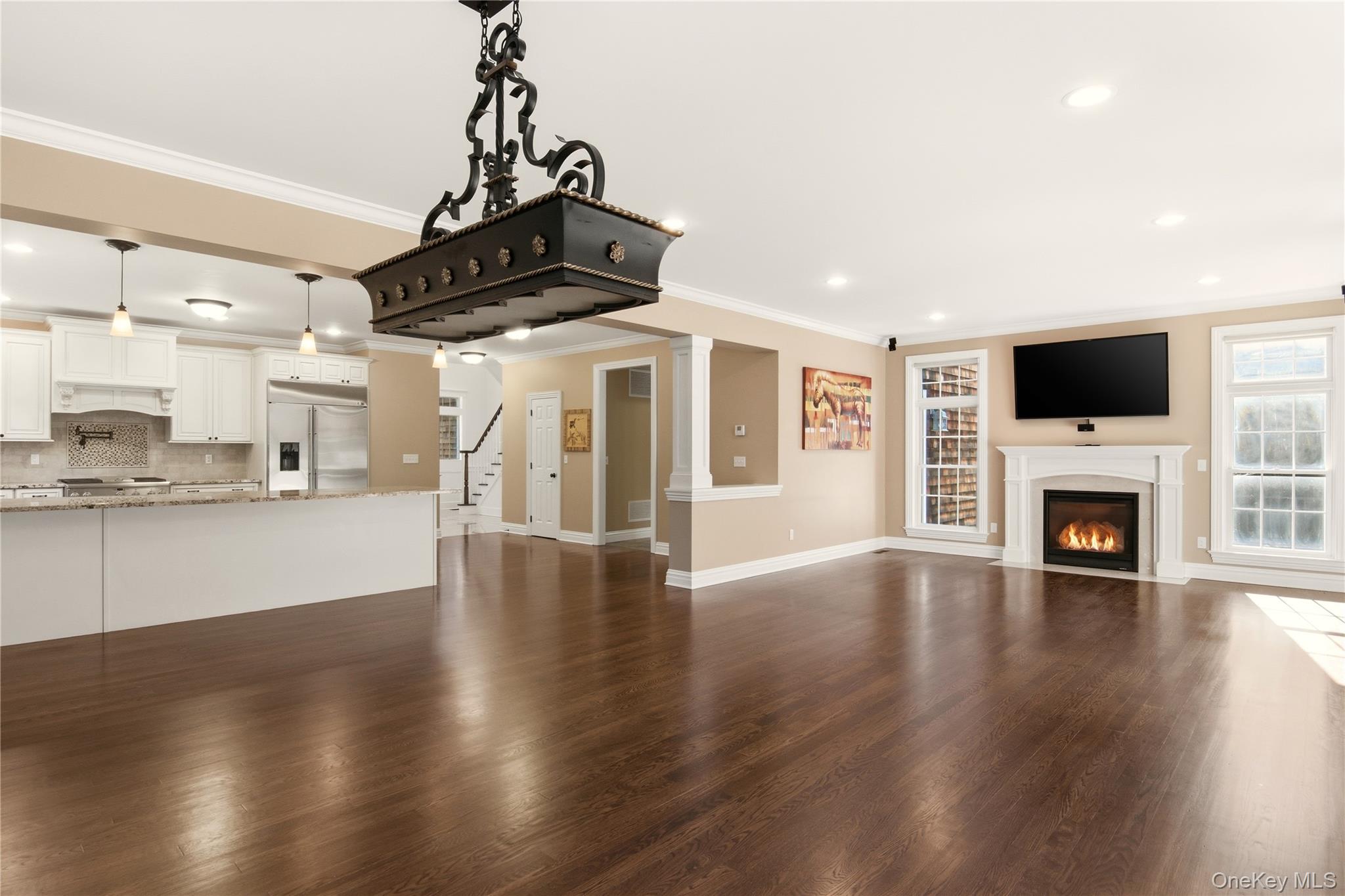69 Old Depot Road Quogue, NY 11959 - Photo 12 of 40 Unfurnished living room with dark wood-type flooring, crown molding, a fireplace with flush hearth, recessed lighting, and stairs