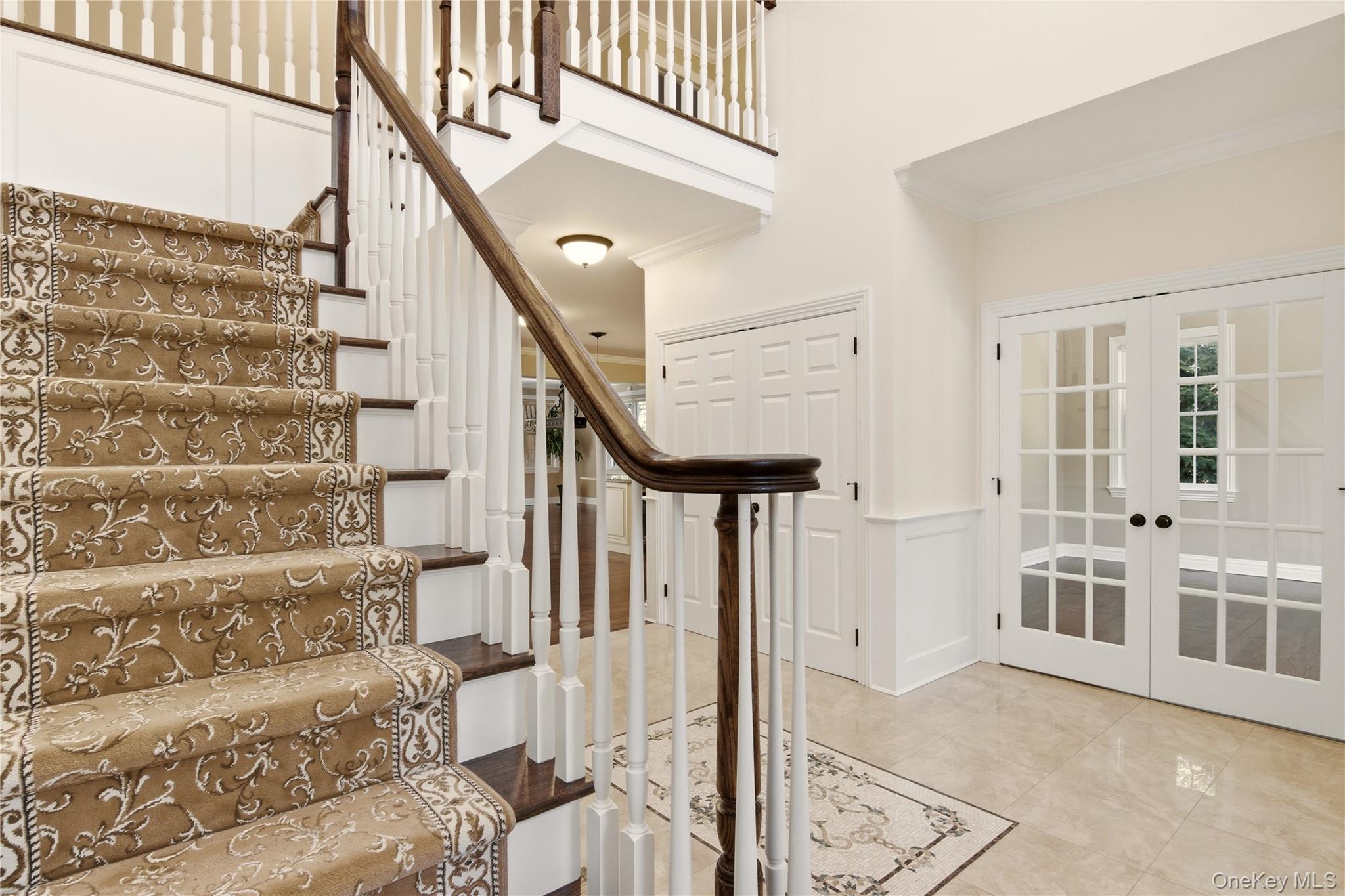 69 Old Depot Road Quogue, NY 11959 - Photo 6 of 40 Staircase featuring a wainscoted wall, a decorative wall, french doors, crown molding, and a towering ceiling