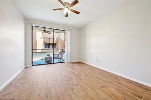 an empty room with wooden floor fan and windows