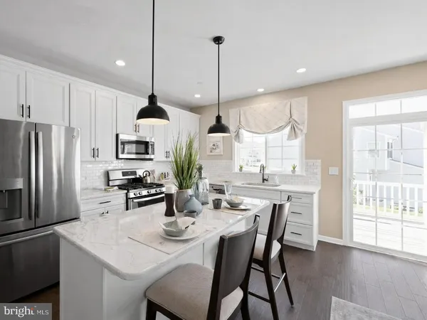 a kitchen with stainless steel appliances kitchen island granite countertop a refrigerator a sink dishwasher a dining table and chairs with wooden floor