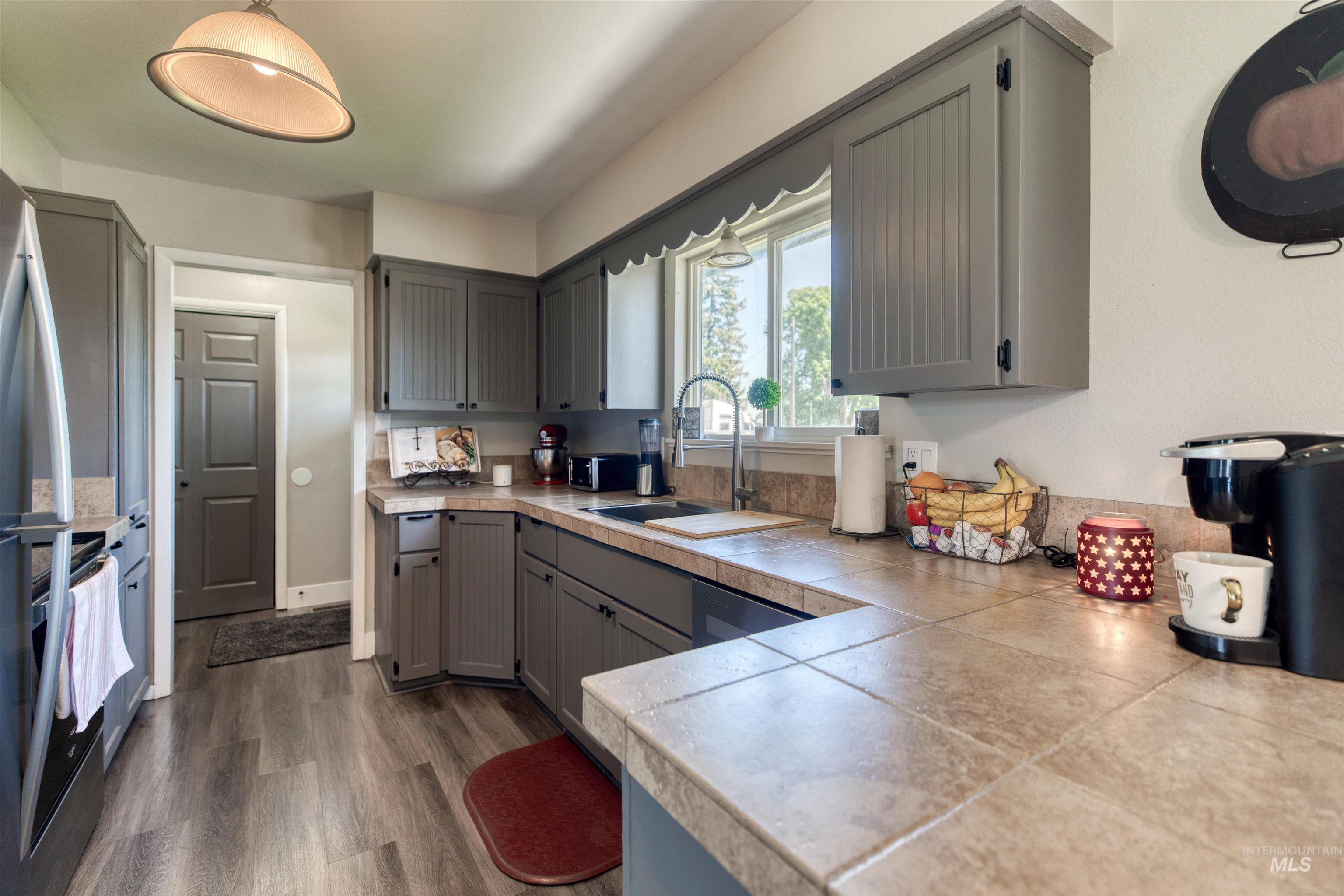 20803 Friends Road Greenleaf, ID 83626 - Photo 6 of 39 Kitchen featuring gray cabinetry, tile countertops with a matching backsplash, a stainless steel sink with a gooseneck faucet, and wood-finish flooring
