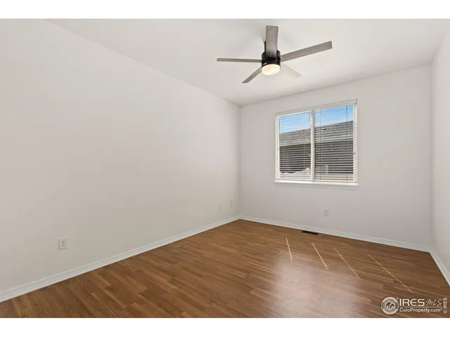 a view of an empty room with wooden floor and a ceiling fan