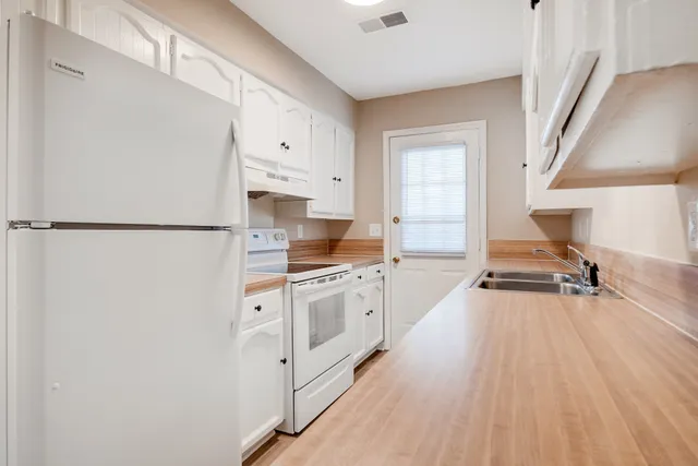 a kitchen with granite countertop a refrigerator a sink dishwasher and white cabinets with wooden floor