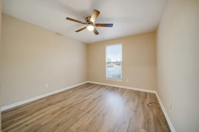 an empty room with wooden floor fan and windows