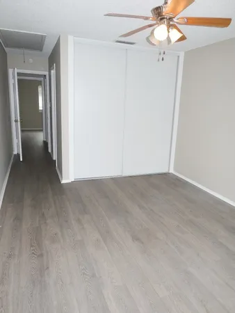 an empty room with a chandelier fan and wooden floor
