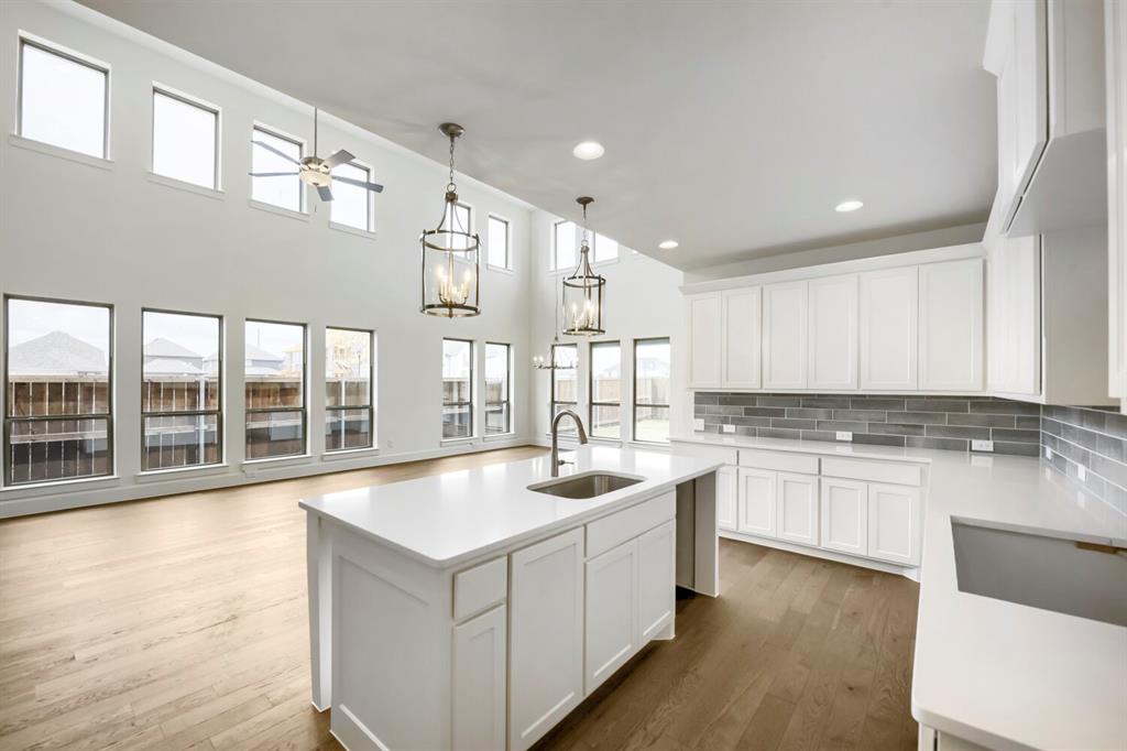 11548 Wulstone Road Haslet, TX 76052 - Photo 9 of 26 Modern kitchen featuring a central island with an undermount sink, white shaker cabinetry, light-toned countertops, and a gray subway tile backsplash
