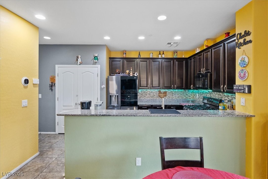 9040 Magnetic Court Las Vegas, NV 89149 - Photo 4 of 43 Kitchen featuring dark brown cabinetry, tasteful backsplash, stainless steel appliances, light stone countertops, and recessed lighting