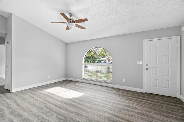 an empty room with wooden floor fan and windows