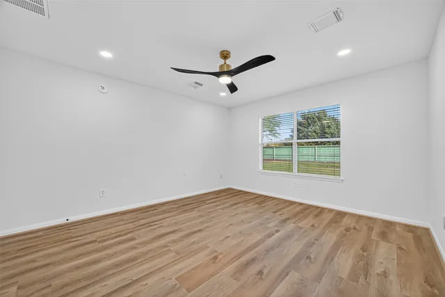 an empty room with wooden floor ceiling fan and windows