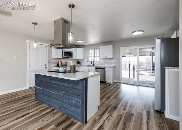 a kitchen with stainless steel appliances granite countertop a stove a sink dishwasher a refrigerator white cabinets and wooden floor