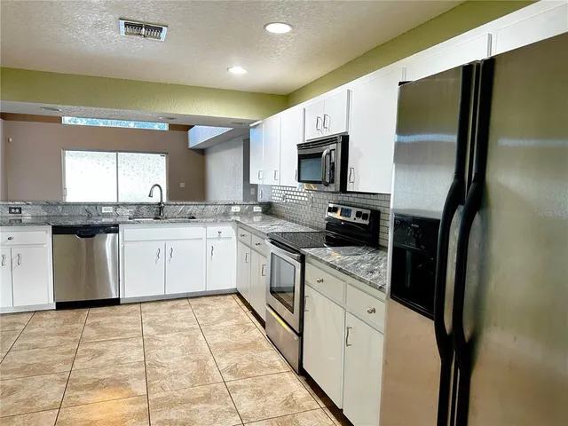a white kitchen with stainless steel appliances granite countertop a stove a sink dishwasher and a refrigerator