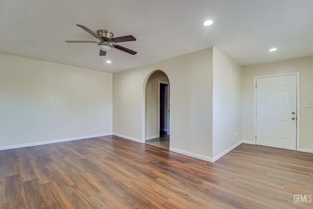 a view of an empty room with wooden floor and a ceiling fan