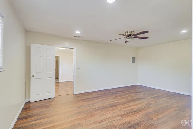a view of an empty room with wooden floor and a ceiling fan