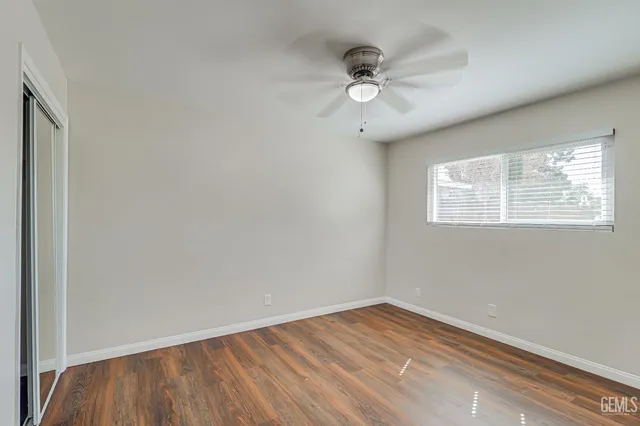 an empty room with wooden floor fan and windows
