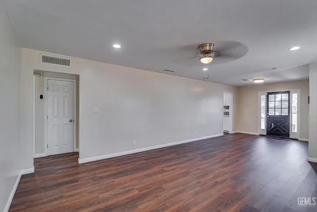 a view of an empty room with wooden floor and a ceiling fan