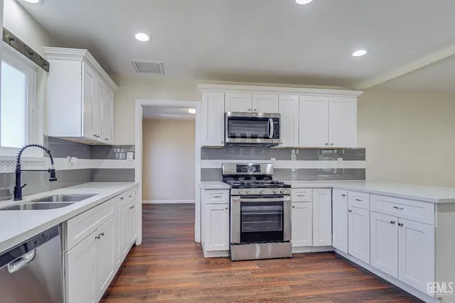 a large kitchen with white cabinets stainless steel appliances and wooden floor