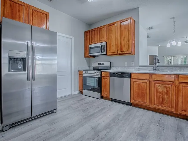 a kitchen with stainless steel appliances granite countertop a refrigerator a sink dishwasher and wooden cabinets with wooden floor